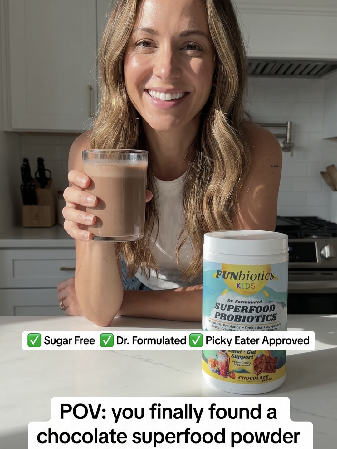 A woman in a kitchen holds a glass of chocolate-colored drink next to a tub of Funbiotics Kids Superfood Probiotics powder. Text overlays highlight product benefits and show a POV statement.